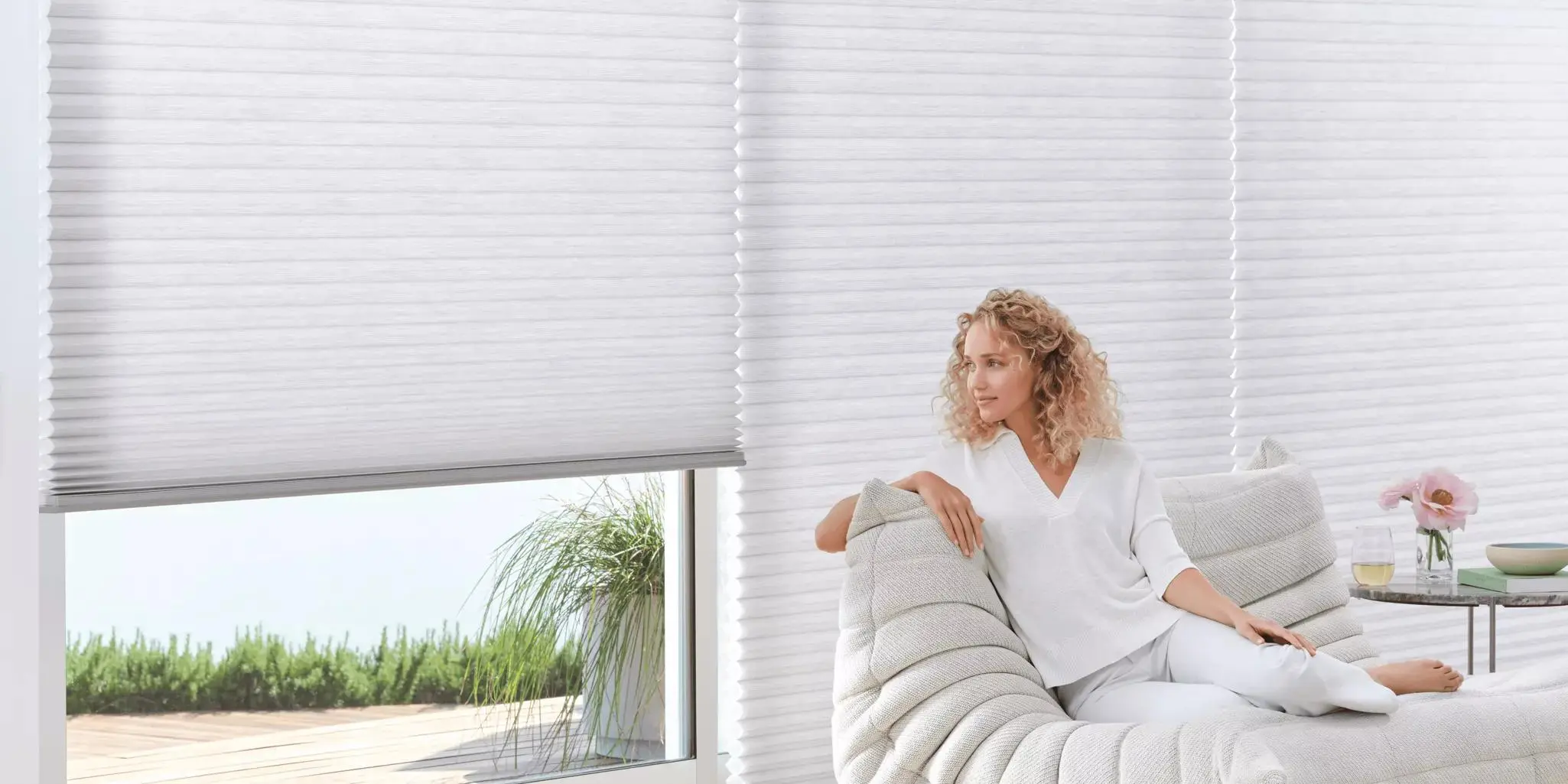 A woman sitting on a chair in front of windows with Hunter Douglas Duette shades.